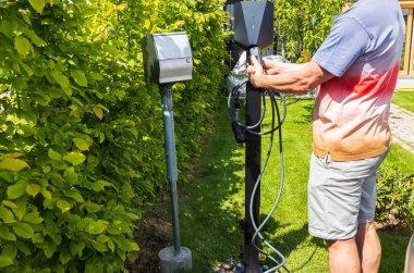 Elektrikli araba şarj istasyonuna kablo bağlayan adamın yakın görüntüsü. İsveç. 