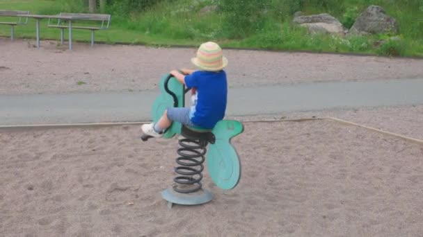 Niedliches Kind Schaukelt Sommertag Auf Spielzeug Motorrad Auf Spielplatz — Stockvideo