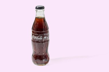 Pembe arka planda izole edilmiş cam bir şişede Coca Cola 'nın yakın görüntüsü. İsveç. Uppsala. 07.07.2021.