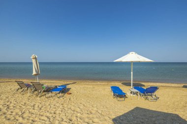 Kumsaldaki şemsiyelerin altındaki boş güneşli yatakların manzarası. Yunanistan