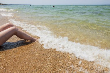 Güzel bir kadın kumsalda oturuyor ve bacakları dalgalanıyor. Yunanistan. 