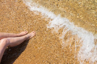 Güzel bir kadın kumsalda oturuyor ve bacakları dalgalanıyor. Yunanistan