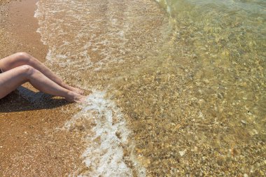 Güzel bir kadın kumsalda oturuyor ve bacakları dalgalanıyor. Yunanistan. 