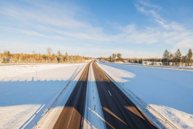 Kış otobanı üzerinde güzel bir manzara. Aydınlık kış gününde kar ve mavi gökyüzüyle kaplı yan tarlalar. İsveç.