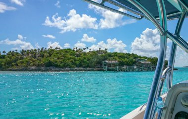 Motorlu tekneden adanın muhteşem manzarası. Turkuaz su ve yeşil ada bitkileri mavi gökyüzünde beyaz bulutların arkasında. Bahamalar. 