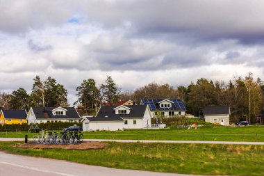 Suburban houses with solar panels and parked bicycles against cloudy spring sky. 