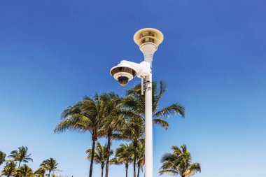 Close up view of security surveillance camera on Ocean Drive with palm trees and clear blue sky on background. Miami Beach. USA.