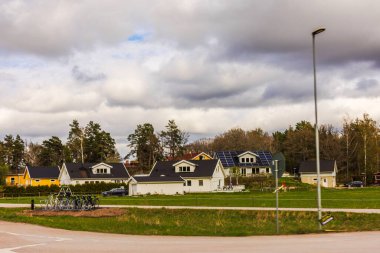 Yeşil çimlerle çevrili güneş panelleri olan ve arka planda bulutlu bahar gökyüzü olan yerleşim evleri. 