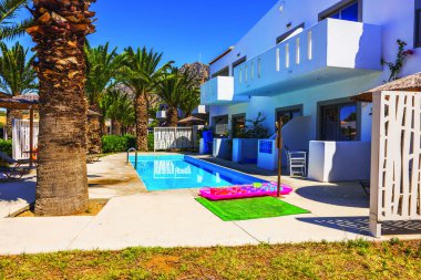 Güneşli yaz gününün arka planında palmiye ağaçları ve dağ bulunan modern otel binası boyunca yüzme havuzunun manzarasını kapat. Yunanistan. Kos.