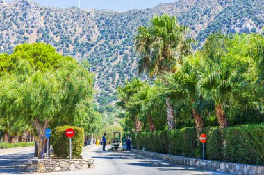 Tatil köyü yolunda küçük traktörleri olan işçiler dağ manzarasının arka planında palmiye ağaçları ve yeşil çalılarla dolu. Yunanistan. Kos. 