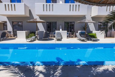 Güneşli yaz gününde otel odalarının yanında yüzme havuzunun yanında güneşli şezlongların ve saman şemsiyelerin güzel manzarası. Yunanistan. Kos.