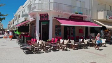 Kardamena 'da Eleftherias Meydanı caddesi boyunca arka planda açık kafelerle yürüyen turistler. Kos. Yunanistan. 