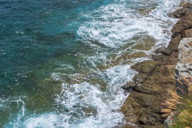 Atlantik Okyanusu 'nun dalgaları kayalık kıyılara çarpıyor. Kıyı kayalıklarının arka planında beyaz köpük ve turkuaz su var. Büyük Kanarya. İspanya.