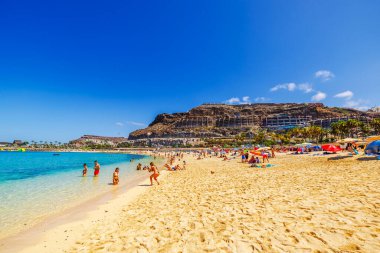 Güneşli Amadores Sahili 'nde turistler altın kumda dinleniyor ve açık Atlantik Okyanusu' nda dağların arkasında yüzüyorlar. Büyük Kanarya. İspanya. 