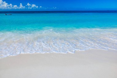 Beyaz bulutlu mavi gökyüzünün arka planında turkuaz Karayip Denizi ile Eagle Beach 'in beyaz kumsalında yuvarlanan küçük okyanus dalgalarının güzel manzarası. Aruba.