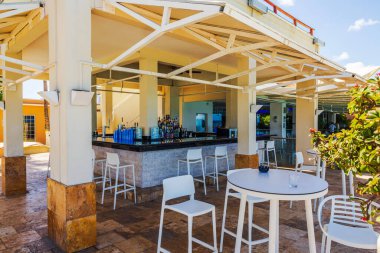 Açık hava plaj barının yakın plan görüntüsü. Arka planda beyaz sandalyeler ve masalar var.. 