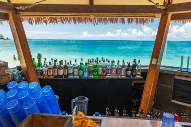 Turkuaz Karayip Denizi ve parlak gökyüzünün arka planında renkli alkol ve mavi bardaklar bulunan tropik sahil barı.. 