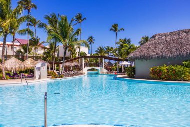Yüksek palmiye ağaçları olan harika bir tatil yeri manzarası ve temiz turkuaz suyun yanında güneşli havanın tadını çıkaran insanlar. Punta Cana. Dominik Cumhuriyeti. 