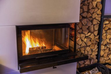 Yanan şöminenin parlak alevleri ve arka planda yakacak odunları olan yakın plan görüntüsü. İsveç.