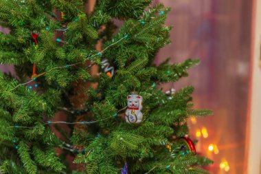 Şanslı kedi süsüsüyle Noel ağacının yakın görüntüsü ve sıcak ev içinde ışıldayan şenlik ışıkları. İsveç.