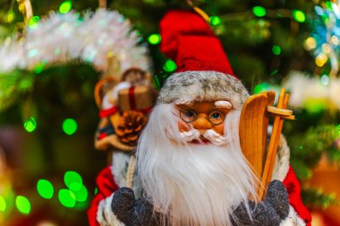 Noel Baba heykelciğinin beyaz sakallı ve arka planda ahşap kayaklı resmi. Noel ağacı ışıkları. İsveç.