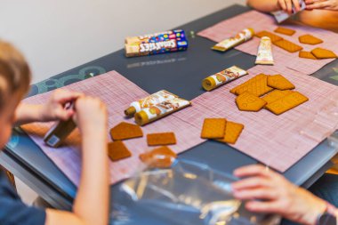 Masada çocukların manzarasını kapatın. Neşeli Noel zanaatı için kremalı zencefilli ekmek evleri hazırlayın.. 