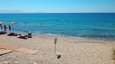 Ege Denizi 'nin çakıl taşı plajının yanında insanların şemsiyelerin altında dinlendiği güzel bir manzara. Yunanistan. Kos. 