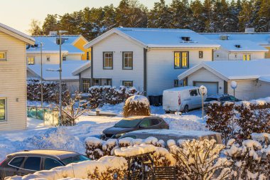Sakin bir banliyöde park etmiş arabaları olan konut villalarının güzel kış manzarası. İsveç.