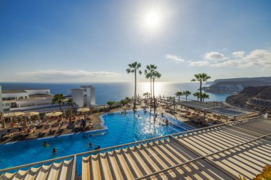 Amadores plajı ve Atlantik Okyanusu 'nun yukarısındaki otel havuzunda parlayan ılık güneş ışığı dinlendirici bir tatil yeri atmosferi yaratıyor. Büyük Kanarya. İspanya.