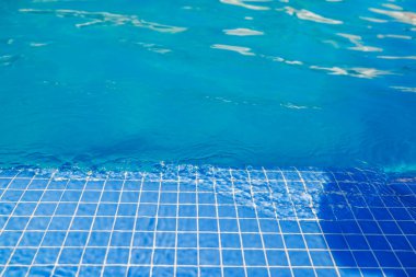 Açık mavi havuz suyunun yumuşak güneş ışığı yansımalarıyla döşenmiş kenarını kapatın. İspanya.