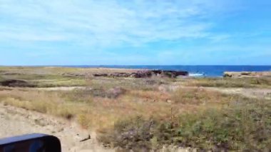 Arka planda Karayip Denizi kıyısı olan Arikok Ulusal Parkı 'ndaki çöl yolunda araba sürüşü görüntüsü. Aruba.