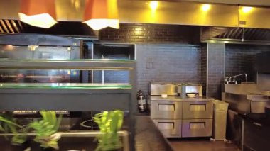 Şefler tezgahın arkasında yemek pişirirken ve metal kaplarda sıcak yemek pişirirken açık mutfak manzarasını kapatın..