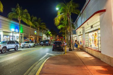 Collins Bulvarı 'ndaki parlayan dükkan vitrinlerinin, palmiye ağaçlarının ve gece trafiğinin güzel manzarası. Miami Plajı. ABD.