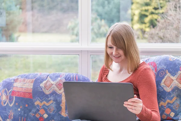 Lachende jonge vrouw is op zoek naar een laptop — Stockfoto
