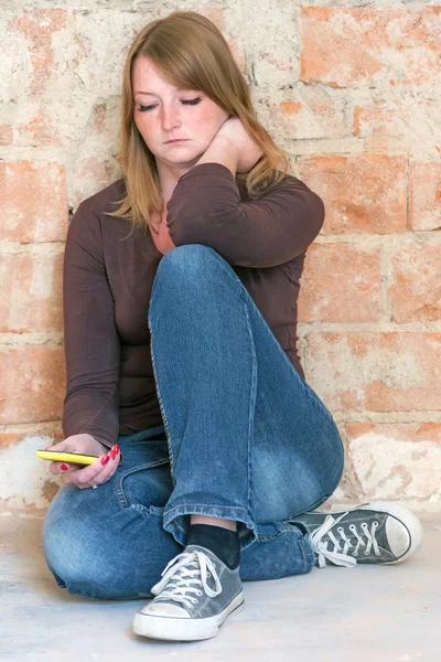 Sitzende junge Frau blickt traurig auf Handy — Stockfoto
