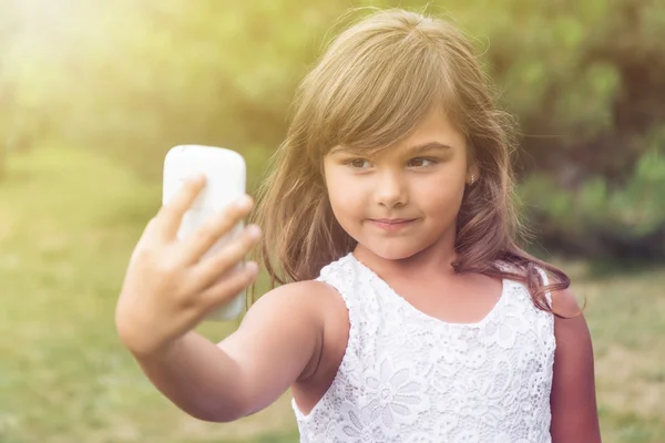 Llittle girl está fazendo selfie ao ar livre . — Fotografia de Stock