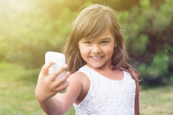 Lächelndes kleines Mädchen macht Selfie und schaut in die Kamera — Stockfoto
