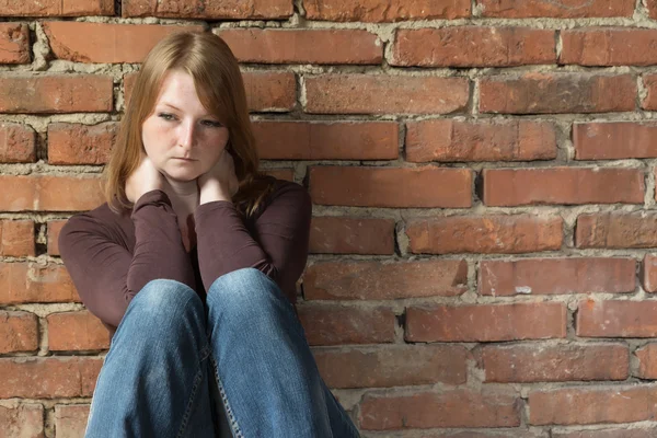 Sitting redhead woman in front of brick wall — Stock Photo, Image