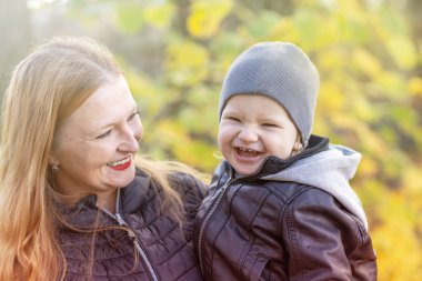 Gülen kızıl saçlı anne ve küçük oğlu sonbahar parkında yakın planda poz veriyorlar..