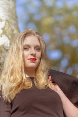 Kameraya gülümseyen çekici bir kızın portresi. Fotoğraf yumuşak sonbahar renklerinde. Dikey.