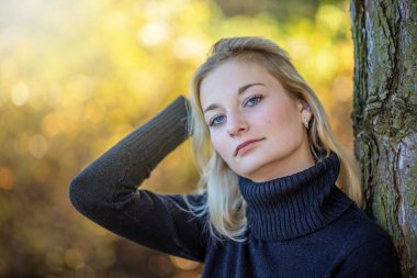 Balıkçı yaka giyen ciddi bir genç kız sonbahar parkında kameraya bakarak poz veriyor. Yatay olarak. 