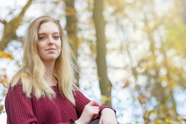 Kırmızı kazak giymiş genç bir kızın kameraya gülümsemesinin alt görüntüsü..