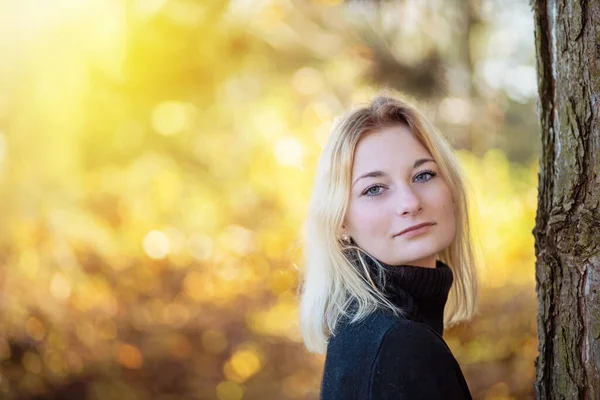 Balıkçı yaka giymiş güzel bir genç kız, sonbahar parkında kameraya bakarak poz veriyor. Yatay olarak. 