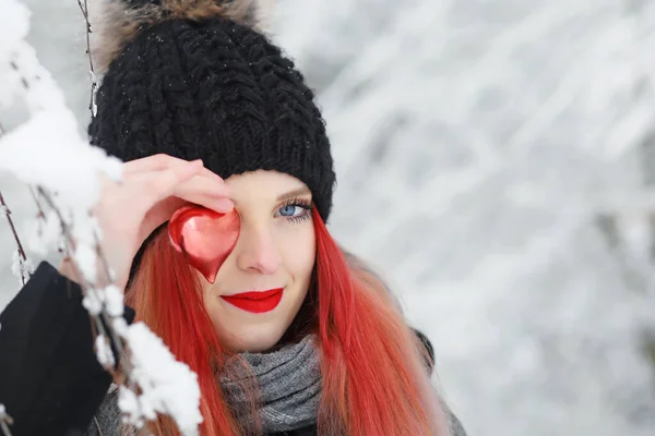 在寒冷的冬日里 一个迷人的红头发姑娘用红心捂住一只眼睛的侧影 — 图库照片