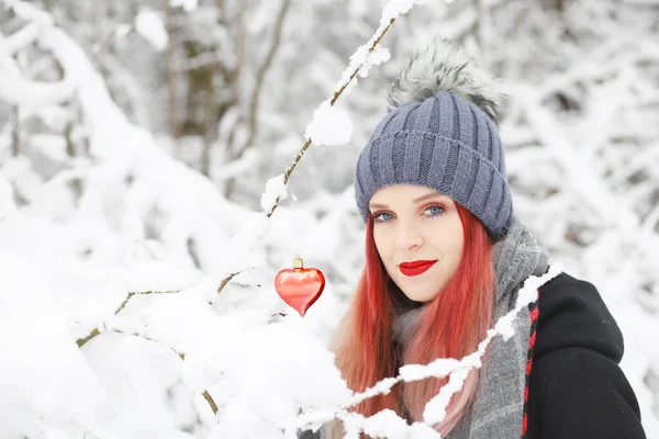 美丽的红头发姑娘的侧影 是红心挂在结冰的雪枝上的姿势 — 图库照片