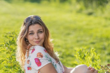 Güzel görünümlü genç kız bir yaz günü dışarıda poz veriyor. Yatay olarak.