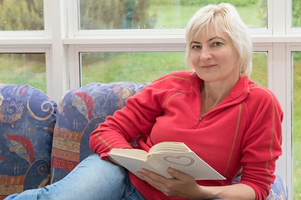 Bionda donna di mezza età è rilassante con un libro in mano — Foto Stock