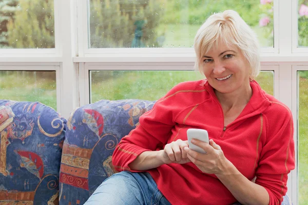 Loira de meia-idade mulher está segurando um telefone celular — Fotografia de Stock