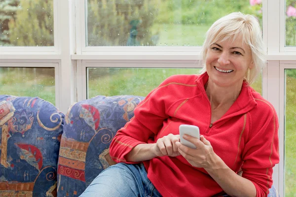 Lachen van middelbare leeftijd vrouw met een mobiele telefoon in haar handen. — Stockfoto