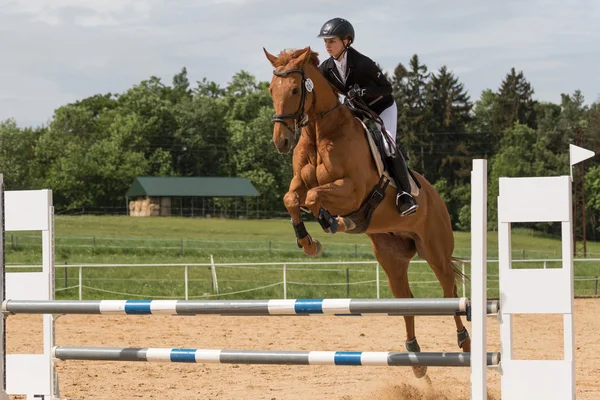 Giovane donna di cavallo sta saltando oltre l'ostacolo — Foto Stock